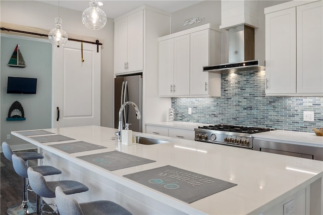 kitchen with appliances with stainless steel finishes, wall chimney exhaust hood, decorative light fixtures, a kitchen island with sink, and a barn door