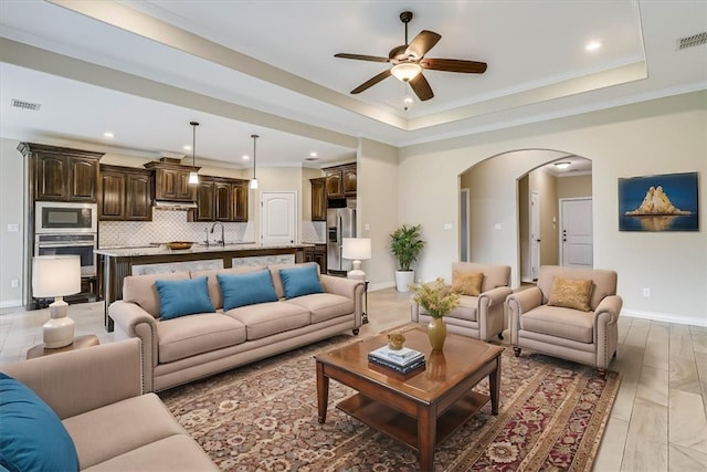 living room with sink, crown molding, light hardwood / wood-style flooring, ceiling fan, and a raised ceiling