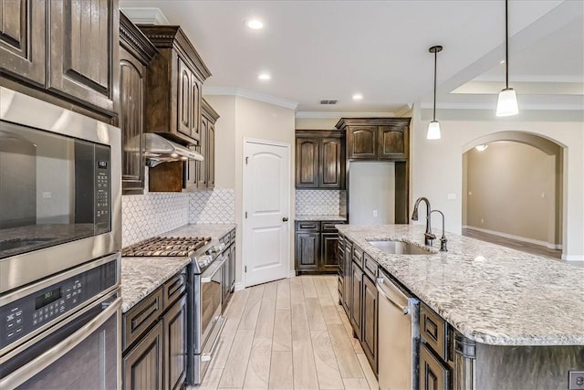 kitchen with sink, appliances with stainless steel finishes, hanging light fixtures, dark brown cabinetry, and a center island with sink