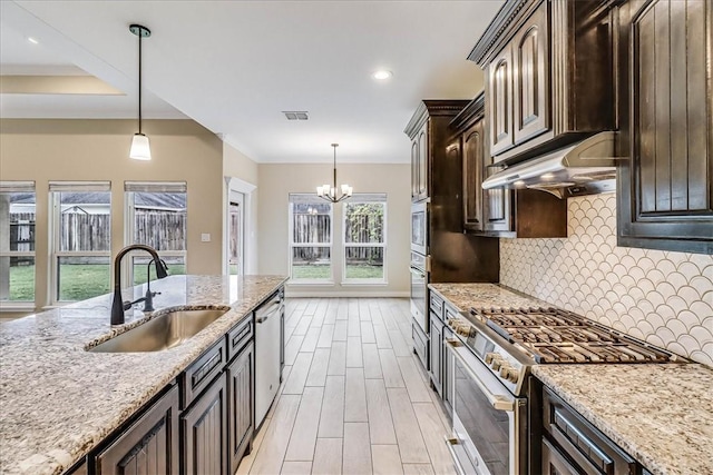 kitchen with appliances with stainless steel finishes, sink, light stone counters, and dark brown cabinetry