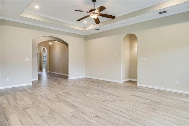 unfurnished room featuring ceiling fan, light wood-type flooring, and a tray ceiling