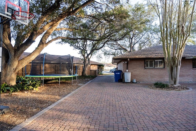 view of home's exterior featuring brick siding, a trampoline, fence, and decorative driveway