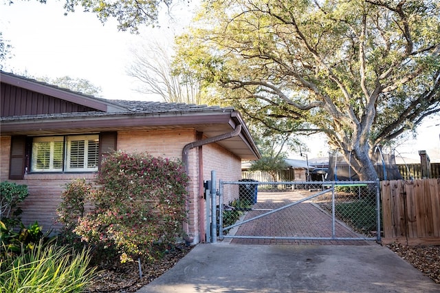 view of side of property with a gate, brick siding, and fence