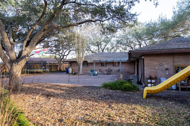 rear view of house with a trampoline, a patio area, fence, and a playground