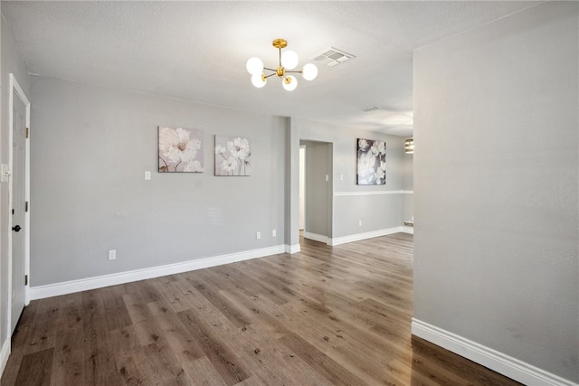 empty room with a textured ceiling, wood-type flooring, and a chandelier