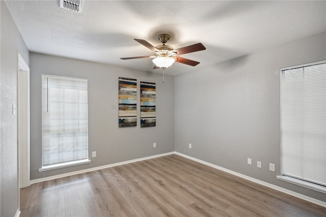 unfurnished room featuring a wealth of natural light, ceiling fan, a textured ceiling, and light hardwood / wood-style floors