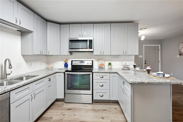 kitchen featuring stainless steel appliances, light wood-type flooring, light stone countertops, sink, and kitchen peninsula