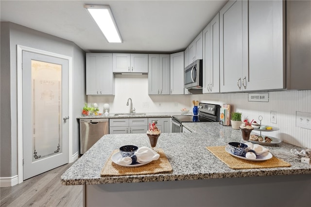 kitchen featuring stainless steel appliances, sink, light hardwood / wood-style flooring, and kitchen peninsula