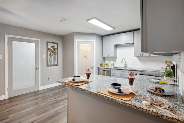 kitchen featuring sink, light stone countertops, light wood-type flooring, stainless steel dishwasher, and black electric stovetop