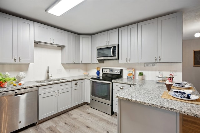 kitchen featuring sink, kitchen peninsula, appliances with stainless steel finishes, light stone countertops, and light wood-type flooring