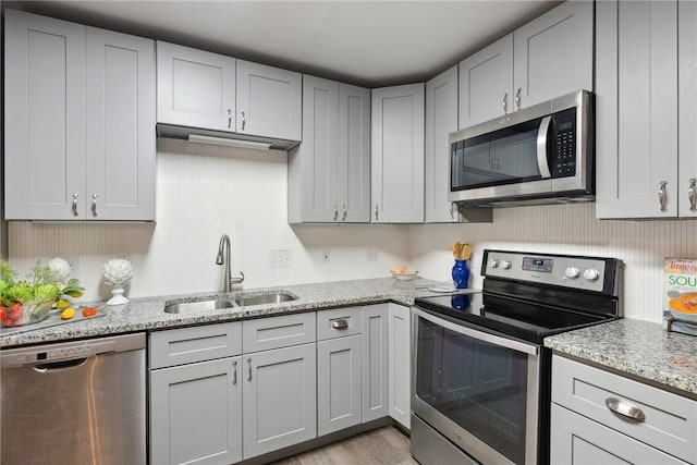 kitchen with stainless steel appliances, light hardwood / wood-style floors, sink, light stone counters, and gray cabinets