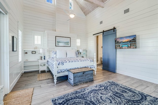 bedroom featuring beam ceiling, a barn door, wood walls, wood finished floors, and high vaulted ceiling