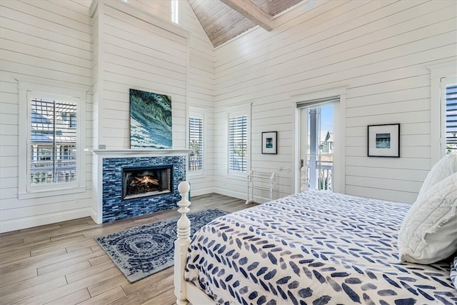 bedroom with high vaulted ceiling, multiple windows, a fireplace, and wood finished floors