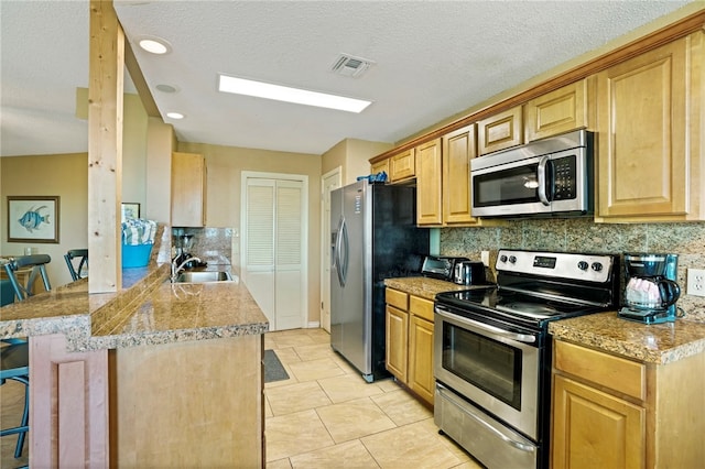 kitchen featuring kitchen peninsula, sink, backsplash, a breakfast bar, and appliances with stainless steel finishes