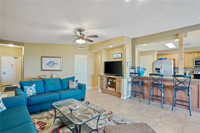 living room with a textured ceiling, ceiling fan, and light tile patterned flooring