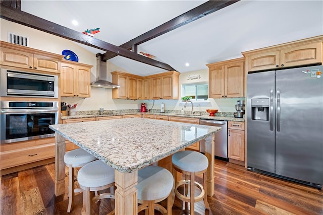 kitchen featuring wall chimney range hood, a breakfast bar, appliances with stainless steel finishes, and a center island