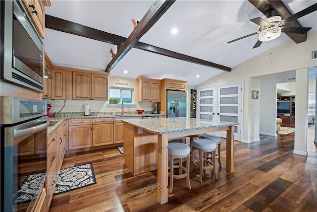 kitchen with stainless steel appliances, vaulted ceiling with beams, a kitchen island, and dark hardwood / wood-style flooring