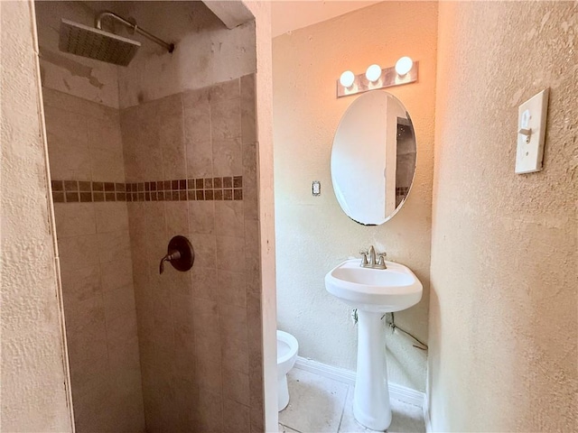 bathroom with toilet, tile patterned flooring, tiled shower, and a textured wall