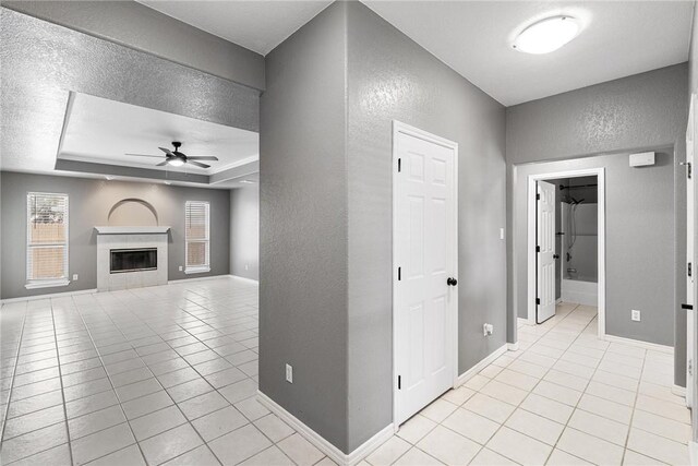 13948 Lighthouse Dr, Corpus Christi, TX 78418 - unfurnished living room featuring a textured wall, a ceiling fan, light tile patterned floors, a tray ceiling, and baseboards