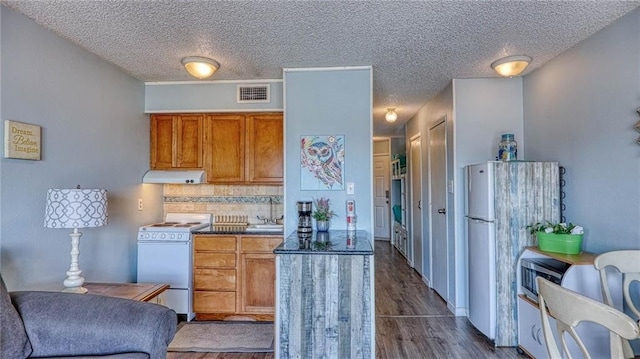 3938 Surfside Blvd Unit 3336, Corpus Christi, TX 78402 - kitchen with white appliances, under cabinet range hood, brown cabinetry, dark wood-style floors, and tasteful backsplash