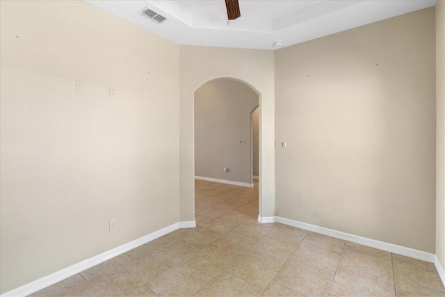spare room with arched walkways, a tray ceiling, baseboards, and visible vents