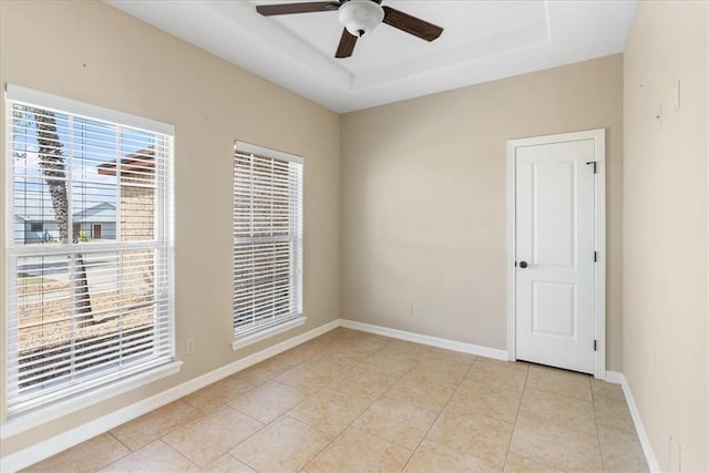 unfurnished room with light tile patterned flooring, a tray ceiling, baseboards, and ceiling fan