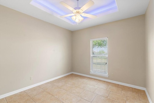 empty room with baseboards, a raised ceiling, light tile patterned floors, and a ceiling fan