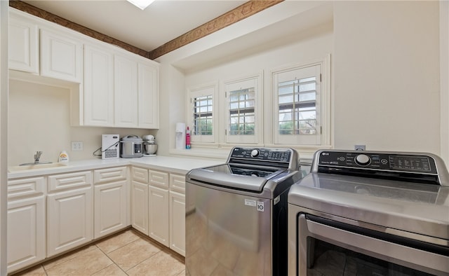 clothes washing area with sink, washing machine and dryer, cabinets, and light tile patterned flooring