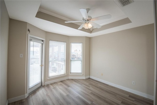 unfurnished room featuring wood finished floors, baseboards, visible vents, a ceiling fan, and a tray ceiling