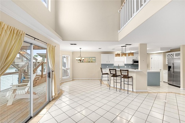 kitchen with light tile patterned floors, appliances with stainless steel finishes, white cabinetry, a kitchen breakfast bar, and a towering ceiling