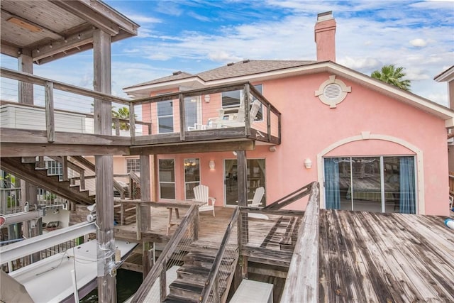 back of property featuring a wooden deck, stairway, a balcony, a chimney, and stucco siding