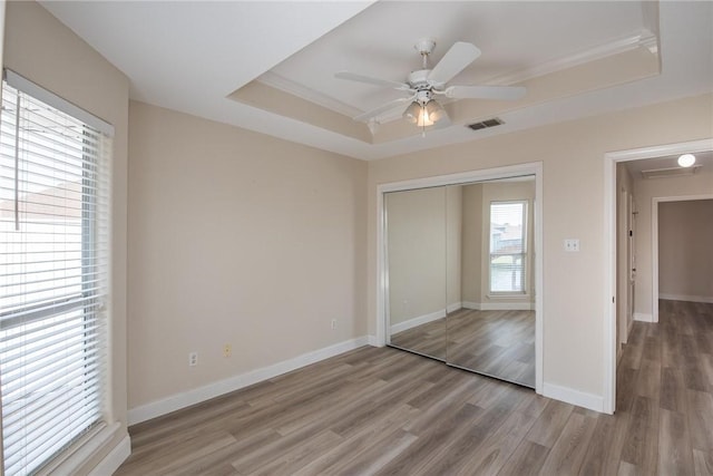 unfurnished bedroom with light wood-style flooring, a closet, baseboards, visible vents, and a tray ceiling