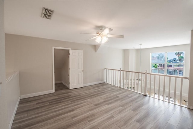 empty room with wood finished floors, a ceiling fan, visible vents, and baseboards