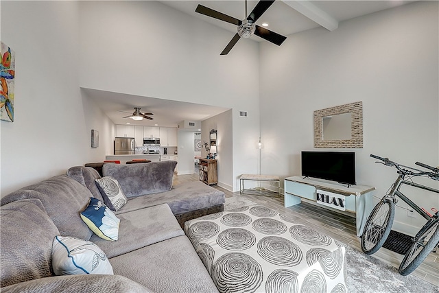 living room featuring a towering ceiling, light hardwood / wood-style floors, ceiling fan, and beam ceiling