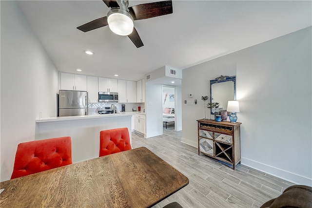 interior space featuring white cabinets, decorative backsplash, light hardwood / wood-style flooring, ceiling fan, and appliances with stainless steel finishes