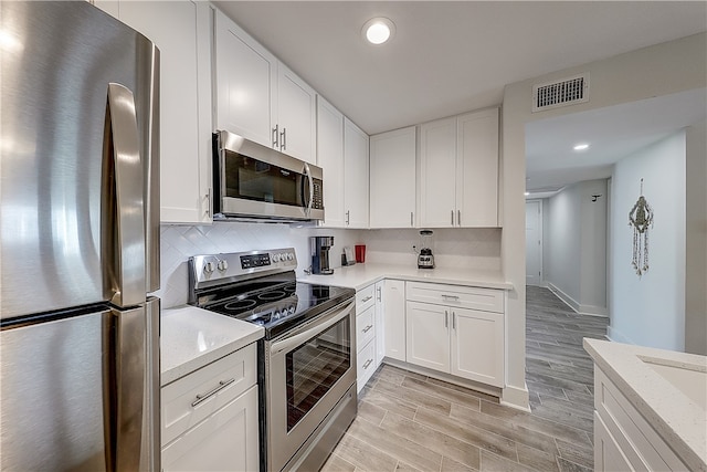 kitchen with white cabinetry, light wood-type flooring, stainless steel appliances, and light stone counters