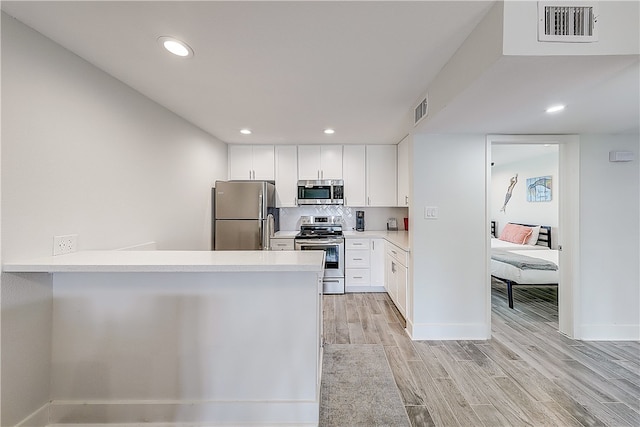 kitchen with stainless steel appliances, white cabinetry, kitchen peninsula, light hardwood / wood-style flooring, and decorative backsplash