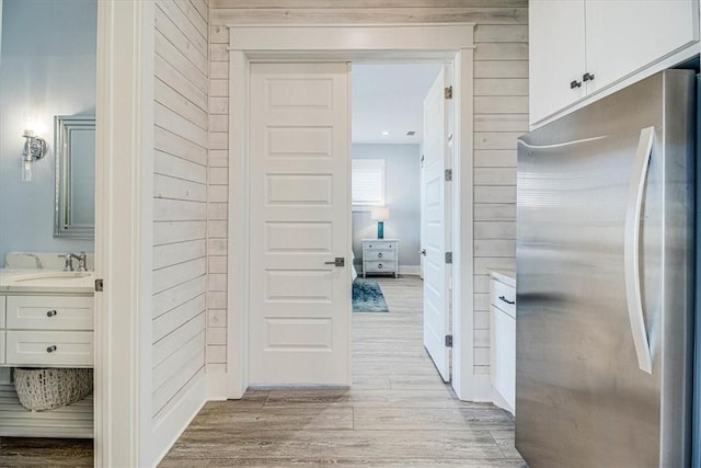 corridor featuring light wood-type flooring, wooden walls, and a sink