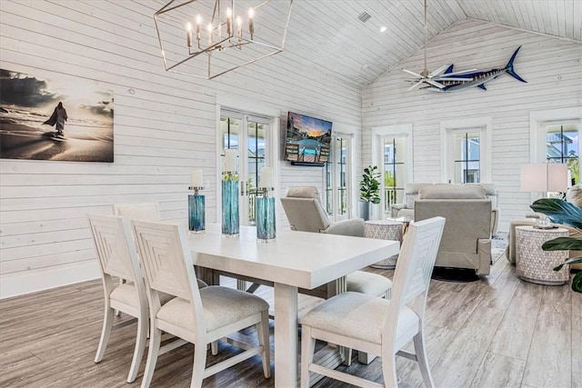 dining room with high vaulted ceiling, wooden walls, wood finished floors, french doors, and an inviting chandelier