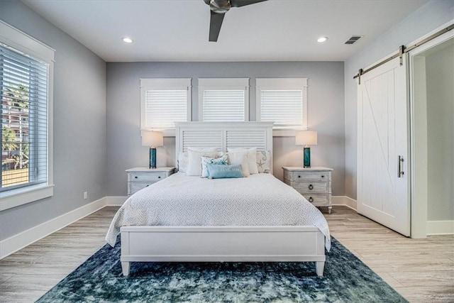 bedroom with a barn door, baseboards, wood finished floors, and recessed lighting