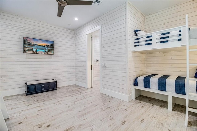 bedroom with a ceiling fan, visible vents, wood walls, and wood finished floors