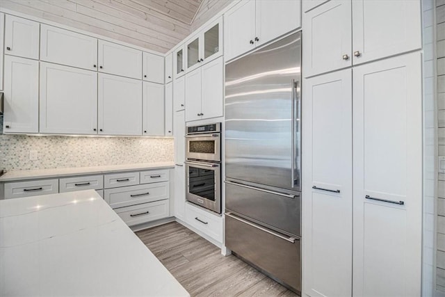 kitchen featuring white cabinetry, appliances with stainless steel finishes, light wood-type flooring, backsplash, and glass insert cabinets