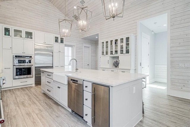 kitchen featuring white cabinets, appliances with stainless steel finishes, a sink, a kitchen island with sink, and a notable chandelier