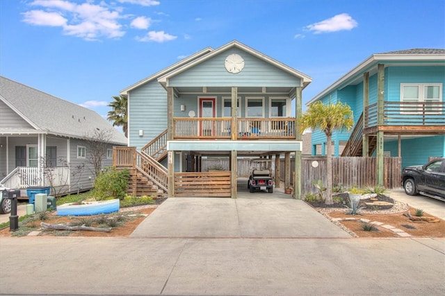 raised beach house featuring a carport, covered porch, concrete driveway, and stairs