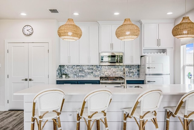 kitchen featuring stainless steel microwave, visible vents, light countertops, freestanding refrigerator, and a sink