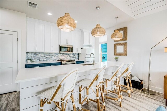 kitchen featuring visible vents, freestanding refrigerator, a sink, stainless steel microwave, and tasteful backsplash