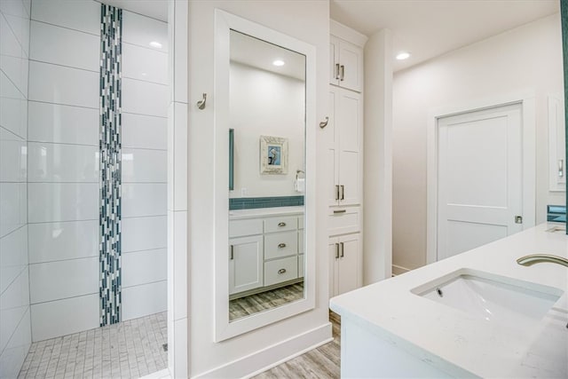 full bath with a walk in shower, double vanity, recessed lighting, wood finished floors, and a sink