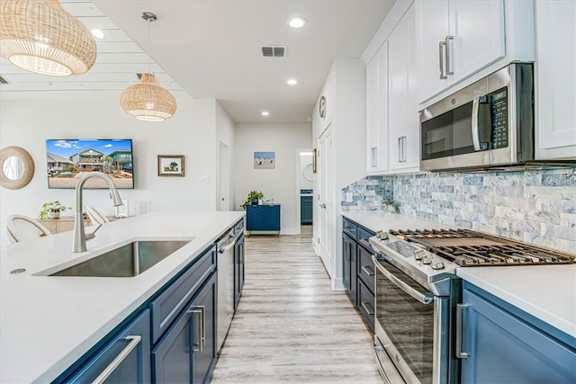 kitchen with a sink, blue cabinetry, backsplash, light wood-style floors, and appliances with stainless steel finishes