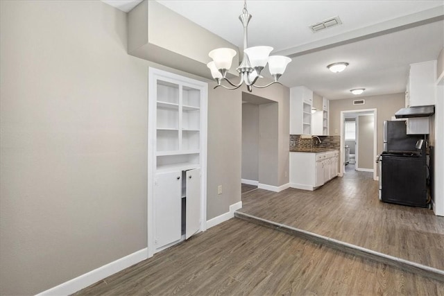 kitchen featuring black range with electric stovetop, decorative light fixtures, tasteful backsplash, a notable chandelier, and white cabinetry