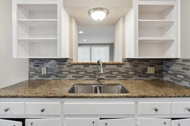 kitchen with backsplash, white cabinets, dark stone countertops, and sink